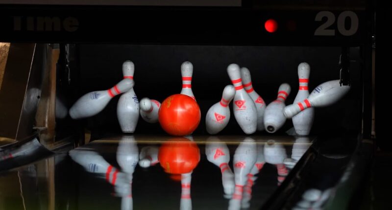 A red bowling ball knocks down a line of white pins